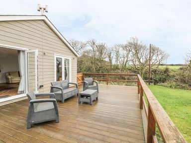An outdoor wooden deck with gray patio furniture and a view of trees and grass at Nant Y Felin Lodge in Aberdaron