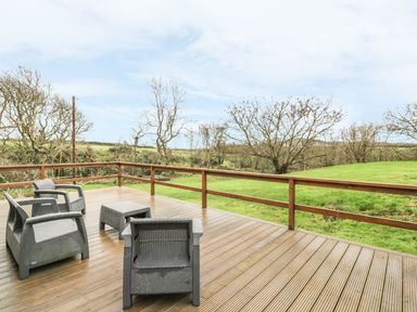 An outdoor wooden deck with four gray chairs and a small table overlooking grassy land and leafless trees at Nant Y Felin Lodge in Aberdaron