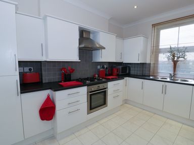 A kitchen with white cabinets black countertops and red kitchen accessories at Apartment 3 Marian Y Mor in Pwllheli