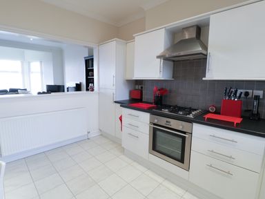 A kitchen with white cabinets black countertop a stove oven and red kitchen utensils at Apartment 3 Marian Y Mor in Pwllheli