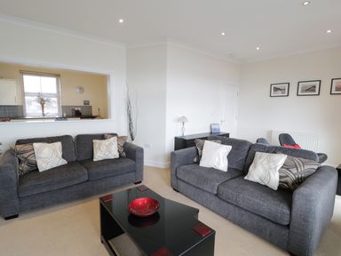 A living room with two gray sofas and a black coffee table with a red bowl at Apartment 3 Marian Y Mor in Pwllheli