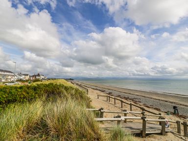 A sandy beach with wooden railings alongside a row of houses and grassy dunes at Apartment 3 Marian Y Mor in Pwllheli