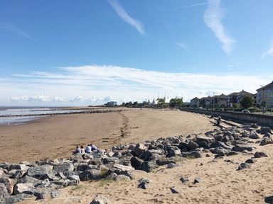 A beach with rocks and people sitting on them near a seawall with buildings in the background at No 9 Watchet
