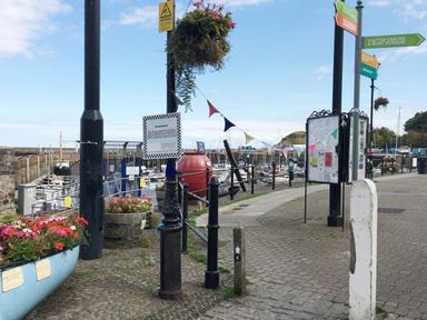 A harbor area with boats docked along the water pathway and signs directing to visitor centre boat museum and West Beach boat school at No 9 Watchet