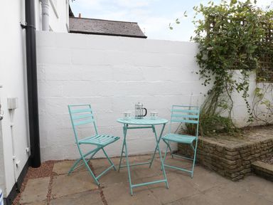 A small patio with two turquoise metal chairs and a round table with a coffee pot and mugs near a white wall with plants at No 9 Watchet