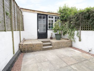 A small enclosed patio with stone steps leading to a door with windows and two potted plants at No 9 Watchet