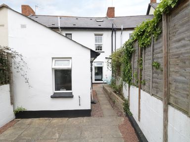 A narrow backyard with stone paving gravel and a white building and wooden fence at No 9 in Watchet