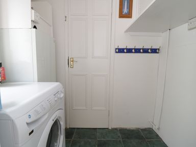 A laundry room with a washing machine a white door wall hooks and a tiled floor at No 9 Watchet
