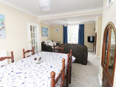 A dining area with wooden chairs and tablecloth by a living area with leather sofas and a wall-mounted television at No 9 in Watchet