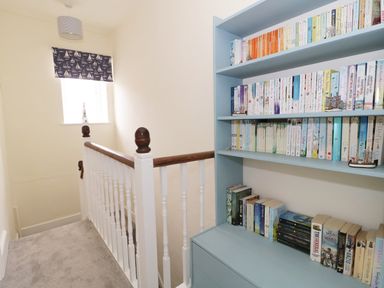 A staircase landing with a bookcase filled with books and a small window with a curtain with a sailboat pattern at No 9 Watchet