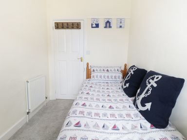A small bedroom with a single bed covered in nautical-themed bedding and two anchor pillows at No 9 in Watchet