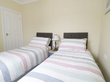 A bedroom with two single beds with striped bedding and a nightstand with a lamp between them at No 9 Watchet