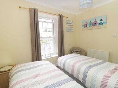 A bedroom with two single beds with striped bedding a window with curtains and beach huts artwork at No 9 Watchet