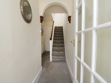 A hallway with carpeted stairs a white door a round wall mirror and a glass panel door at No 9 in Watchet