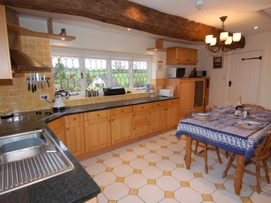A kitchen with wooden cabinets a dining table set with plates and glasses and a window with a countryside view at Appletree Cottage in Higher Brimley near Bovey Tracey