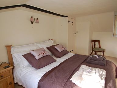 A bedroom with a bed, pillows, towels, a wooden nightstand, a chair, and a door at Appletree Cottage in Higher Brimley near Bovey Tracey