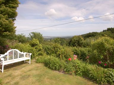 A garden with a white bench and flowering plants overlooking a valley at Appletree Cottage in Higher Brimley near Bovey Tracey
