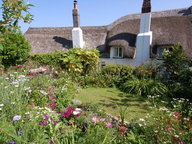 A garden with flowers and bushes in front of a thatched cottage at Appletree Cottage in Higher Brimley near Bovey Tracey