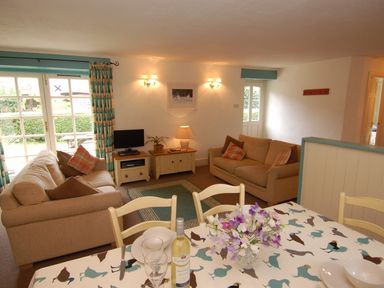 A living room with two beige sofas a small television and a dining table with flowers at The Coach House in Ugborough