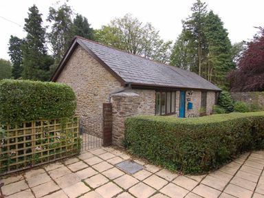 Stone cottage with blue door and windows surrounded by hedges and trees at The Coach House in Ugborough