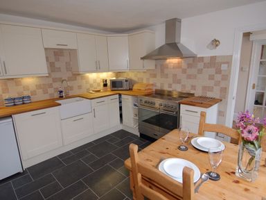A kitchen with white cabinets wooden countertops a dining table set with plates glasses and a vase with flowers at Jordan House in Boscastle