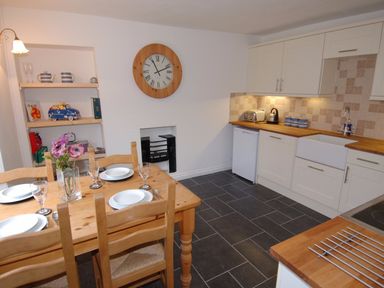 A kitchen with a wooden dining table set for four and white cabinets at Jordan House in Boscastle