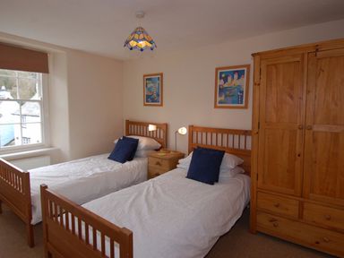 A bedroom with two single beds two blue pillows a wooden wardrobe and a window at Jordan House in Boscastle