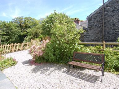 A garden area with a wooden bench gravel path flowering bushes and stone building at Jordan House in Boscastle