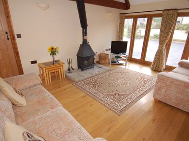 A living room with two sofas a stove a television on a stand and a rug on wooden floor at The Milking Parlour in Wookey