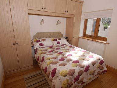 A bedroom with a double bed and built-in wooden wardrobes near a window at The Milking Parlour in Wookey