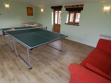 A game room with a ping pong table foosball table and red sofa at The Milking Parlour in Wookey