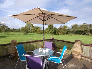 An outdoor patio with a round table four chairs and a large umbrella overlooking a grassy field at The Milking Parlour in Wookey