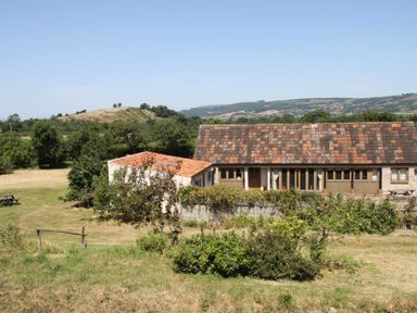 A rural house with a tiled roof surrounded by grass and trees with hills in the background at The Milking Parlour in Wookey