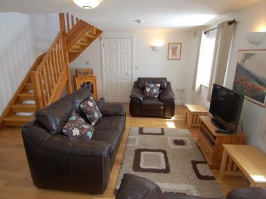 A living room with leather sofas a patterned rug wooden stairs and a television at The Old Cider Barn in Wookey