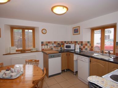 A kitchen with wooden table and chairs dishwasher microwave and sink with windows at The Old Cider Barn in Wookey