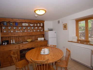 A kitchen with wooden cabinets and dining table with chairs and a refrigerator by the window at The Old Cider Barn in Wookey