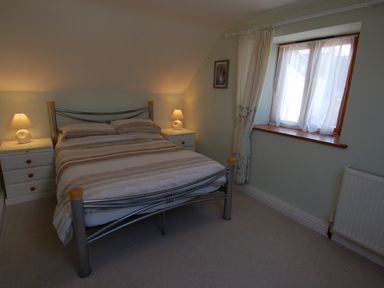 A bedroom with a double bed between two bedside tables with lamps next to a window at The Old Cider Barn in Wookey