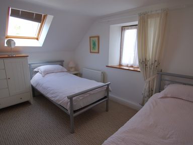 A bedroom with two single beds a window with curtains and a skylight at The Old Cider Barn in Wookey