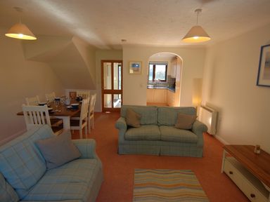 A living room with two sofas and a dining table set with dishes with a view into the kitchen at Pine Cottage in Maenporth
