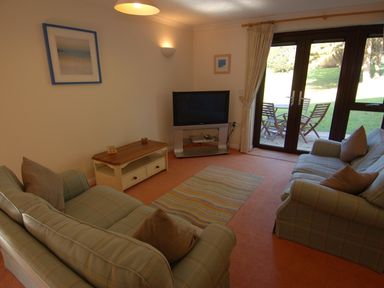 A living room with two sofas a coffee table a television and glass doors leading to a patio at Pine Cottage in Maenporth