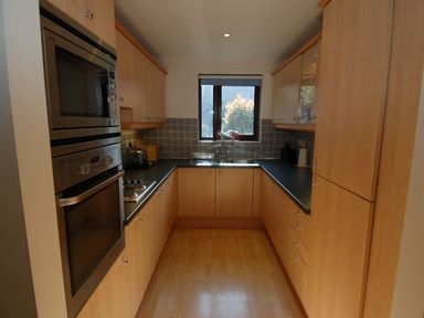 A kitchen with wooden cabinets a double oven a sink below a window and a tiled backsplash at Pine Cottage in Maenporth
