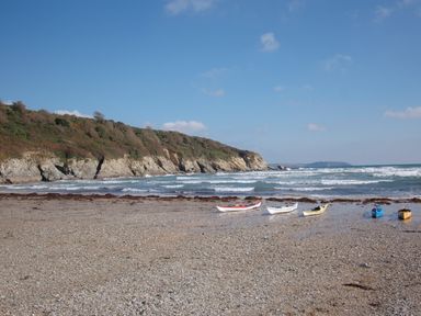 A beach with five kayaks on the shore and waves with cliffs in the background at Pine Cottage in Maenporth