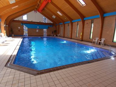 An indoor swimming pool with tiled flooring surrounded by wooden beams and brick walls at Pine Cottage in Maenporth