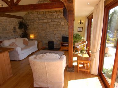 A living room with wooden beams stone wall white sofas and large windows at Sunnyside in Staple Fitzpaine
