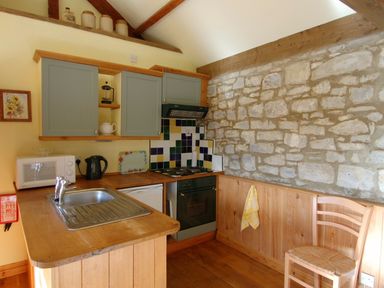 A kitchen with wooden countertops cabinets a stone wall and a wooden chair at Sunnyside in Staple Fitzpaine