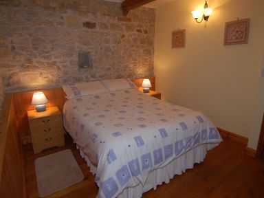 A bedroom with a double bed two bedside tables with lamps wooden flooring and stone and painted walls at Sunnyside in Staple Fitzpaine