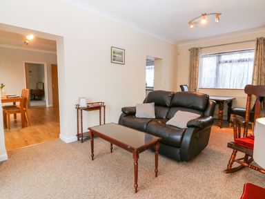 A living room with a black leather sofa, wooden coffee table, side table, and rocking chair at Little Waycroft in Dawlish