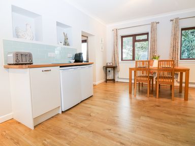 A kitchen area with a toaster coffee maker white cabinets wooden countertop and a wooden dining table with four chairs at Little Waycroft in Dawlish