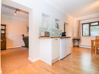 A kitchen area with a toaster coffee machine small fridge and dining table near a window at Little Waycroft in Dawlish