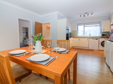 A kitchen with wooden dining table set for four with a vase of flowers and white cabinetry and appliances at Little Waycroft in Dawlish